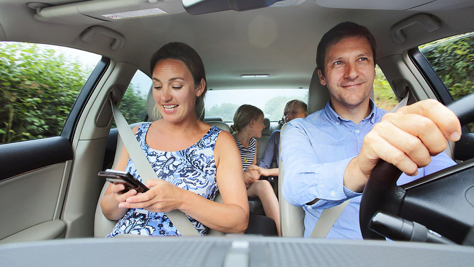 Family in car, mother looking at phone.