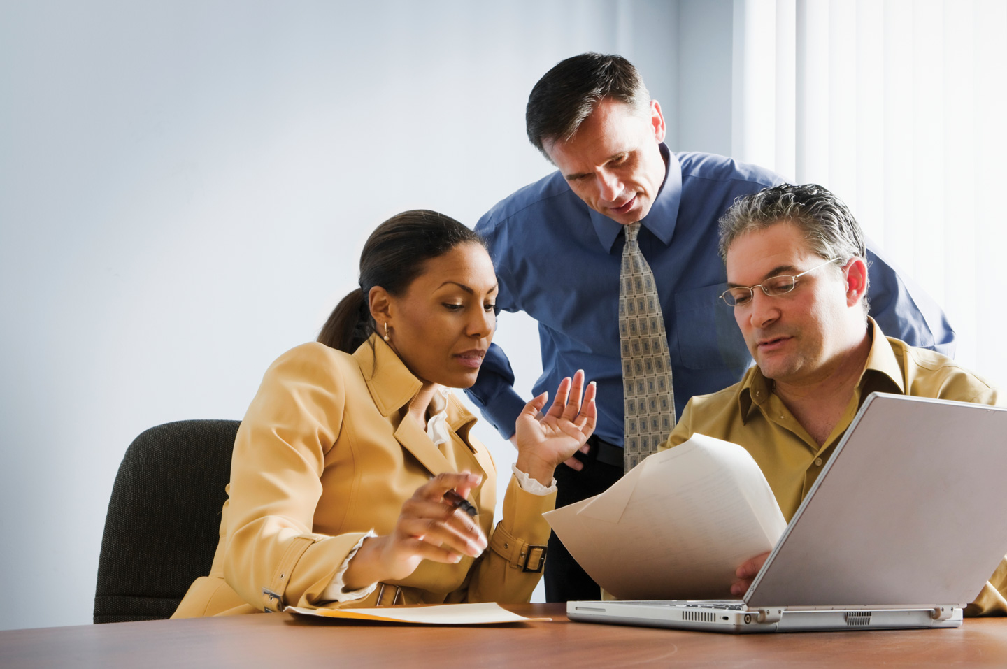 Three business professionals discussing content over a report and laptop.