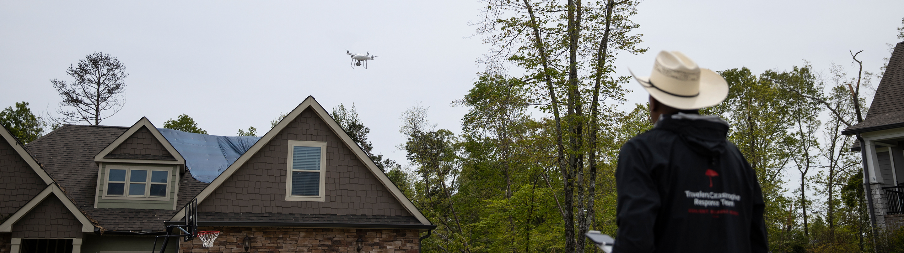 A Travelers property claim agent flying a drone over a home after a storm.