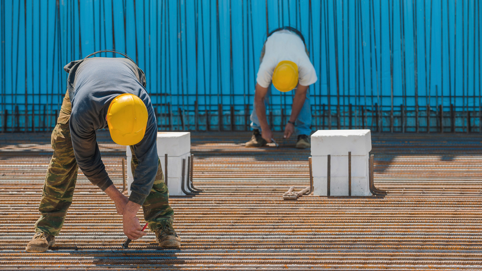 Two construction workers are bent down to work on a construction site.