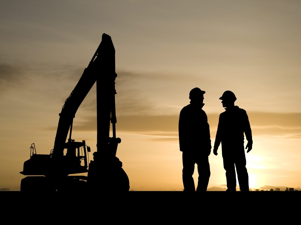 Two silhouetted construction workers and a construction shovel against a sunrise.