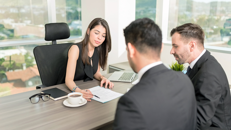 Three people having a meeting in an office and going over a contract.