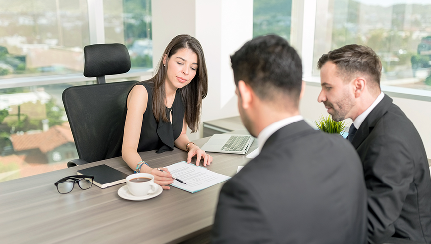 Three people having a meeting in an office and going over a contract.