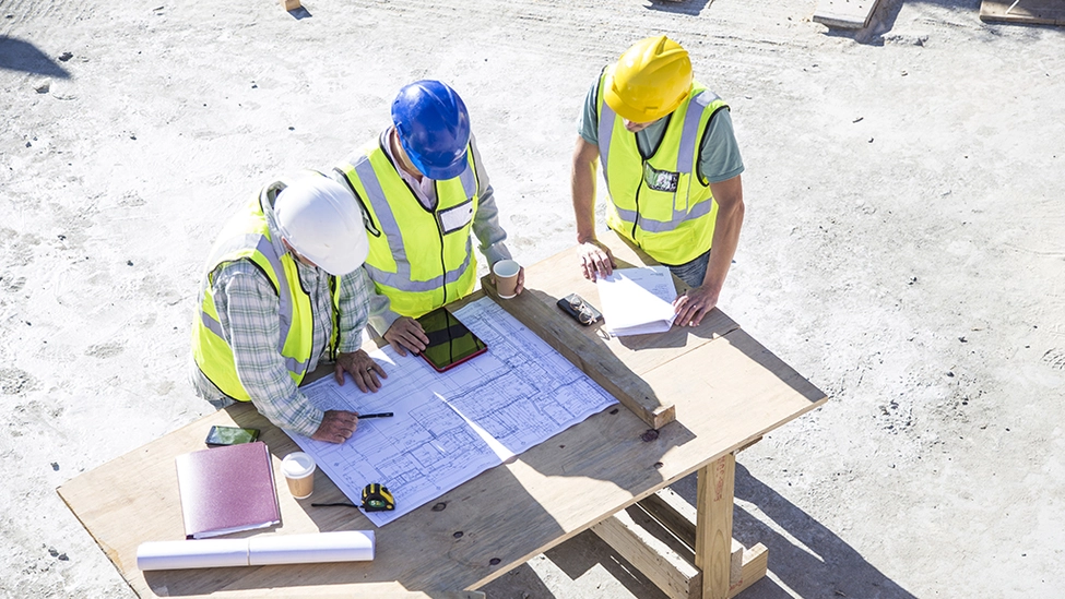 Three construction workers onsite having a meeting and looking at a smart device.