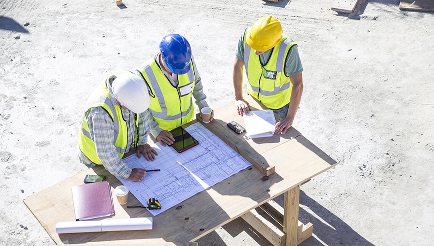 Three construction workers onsite having a meeting and looking at a smart device.