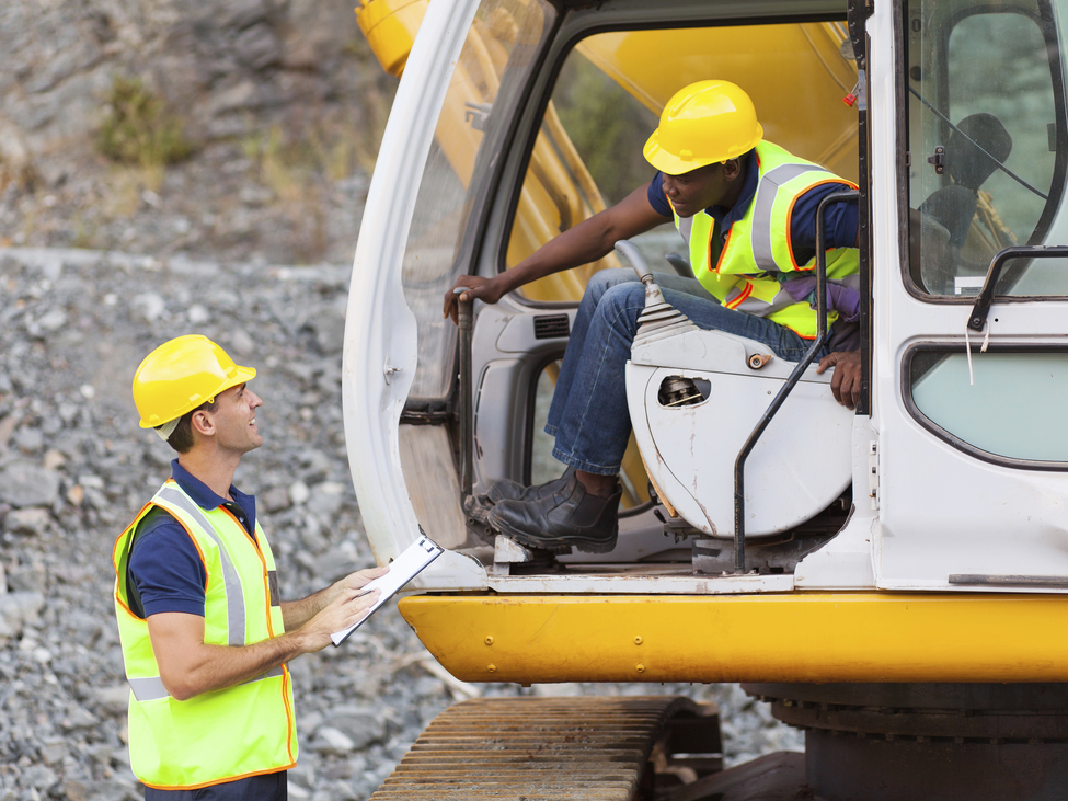 Two construction workers talk about insurance coverage while one is seated on an excavator.