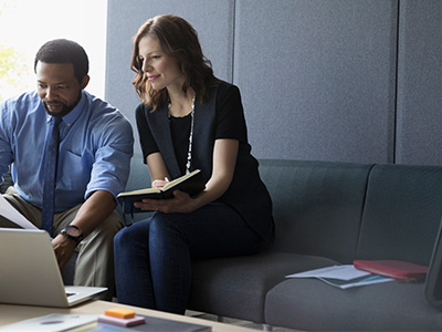 Man and woman in business attire in office conferring over documents.