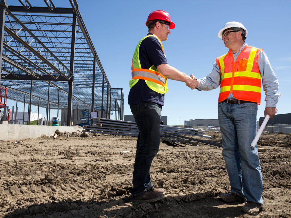 Two construction workers shaking hands at a construction site.