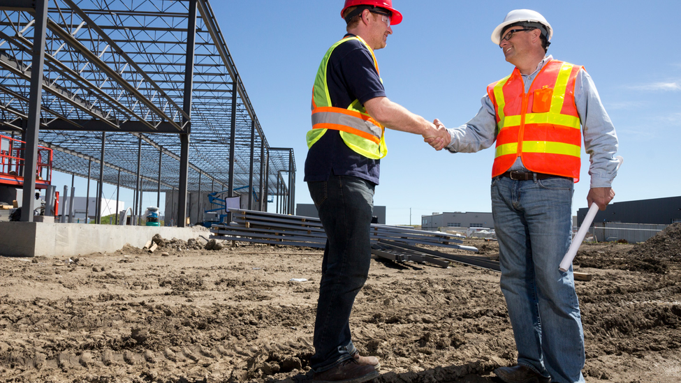 Two construction workers are shaking hands on a construction site.