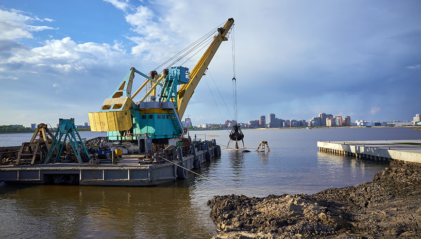 Dredging crane moving debris in water on a floating platform