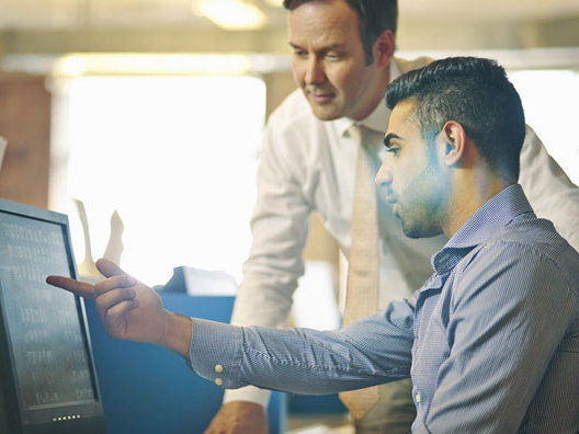 Two men in shirts and ties looking at laptop screen in office.