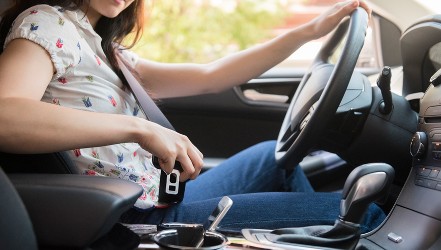 Woman behind the wheel of her car putting her cell phone in the center console.