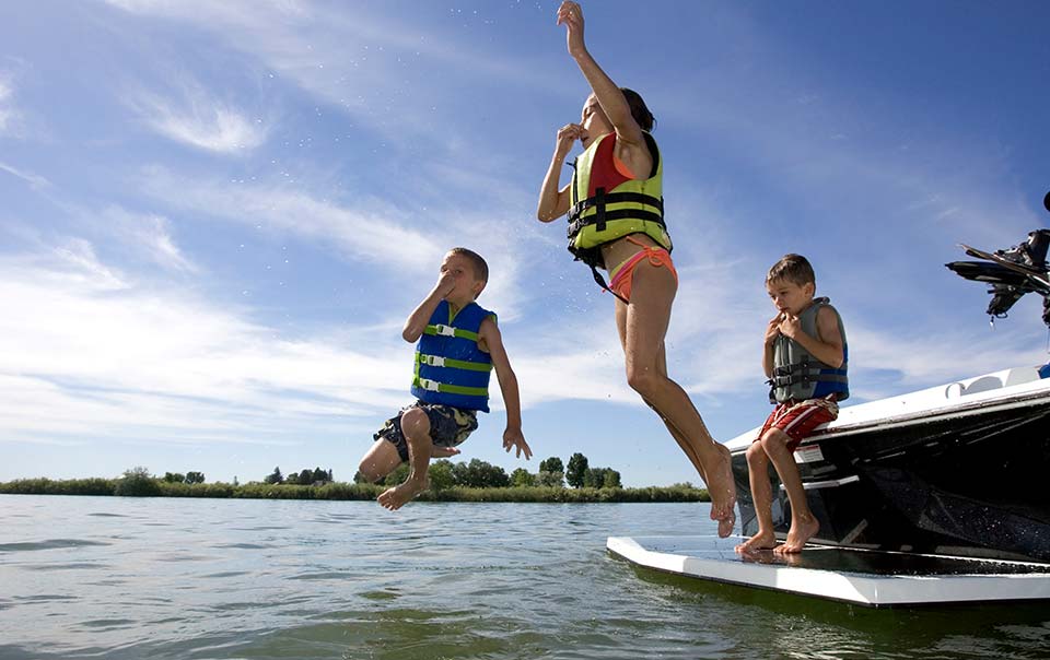 Three children safely jumping into water from a boat.