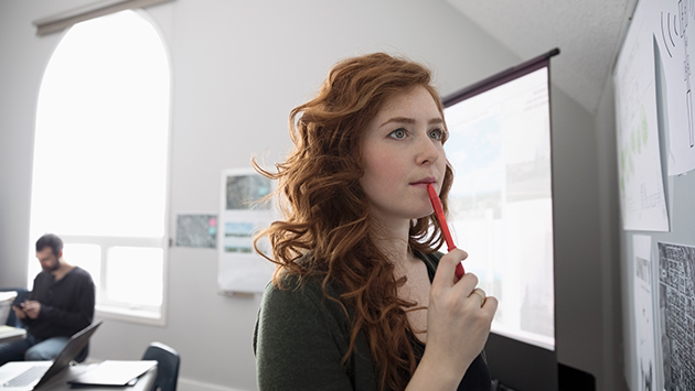 Woman thinking intently looking at a whiteboard.
