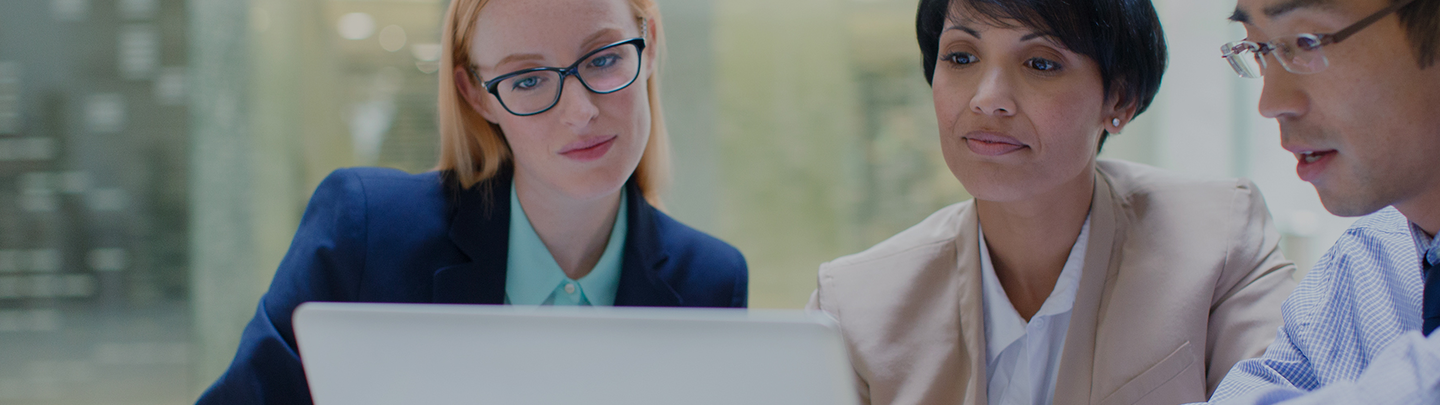 Two women in business suits looking at laptop together in light-filled office.