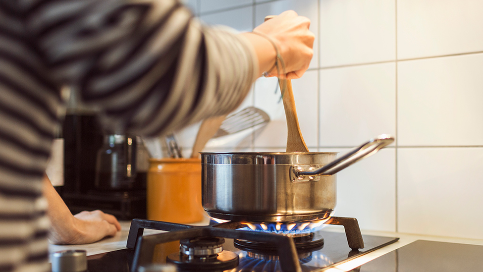 Person stirring food in a pot on a gas stove.