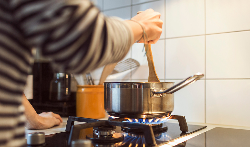 Person stirring food in a pot on a gas stove.
