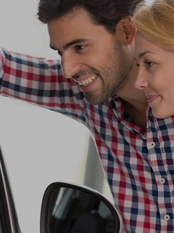 A couple smiles with excitement as they look at a new car.