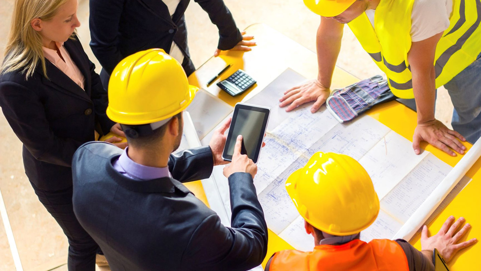 Construction team looking at electronic handheld device and blueprint