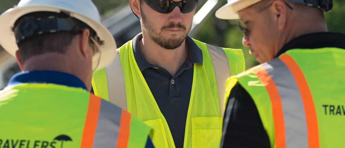 Construction workers in safety gear conferring on work site.