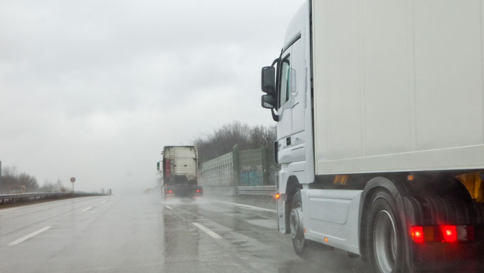 Two commercial trucks driving safely in dangerous weather conditions.