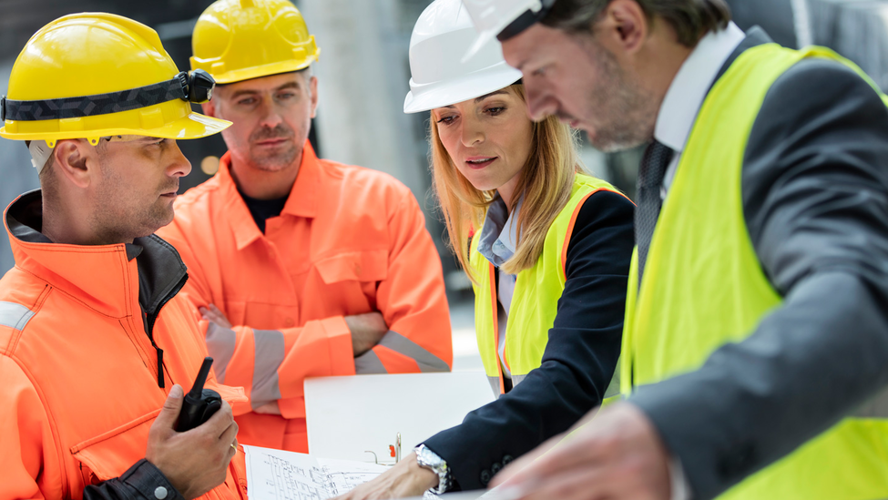 Engineers and construction workers reviewing blueprints at construction site