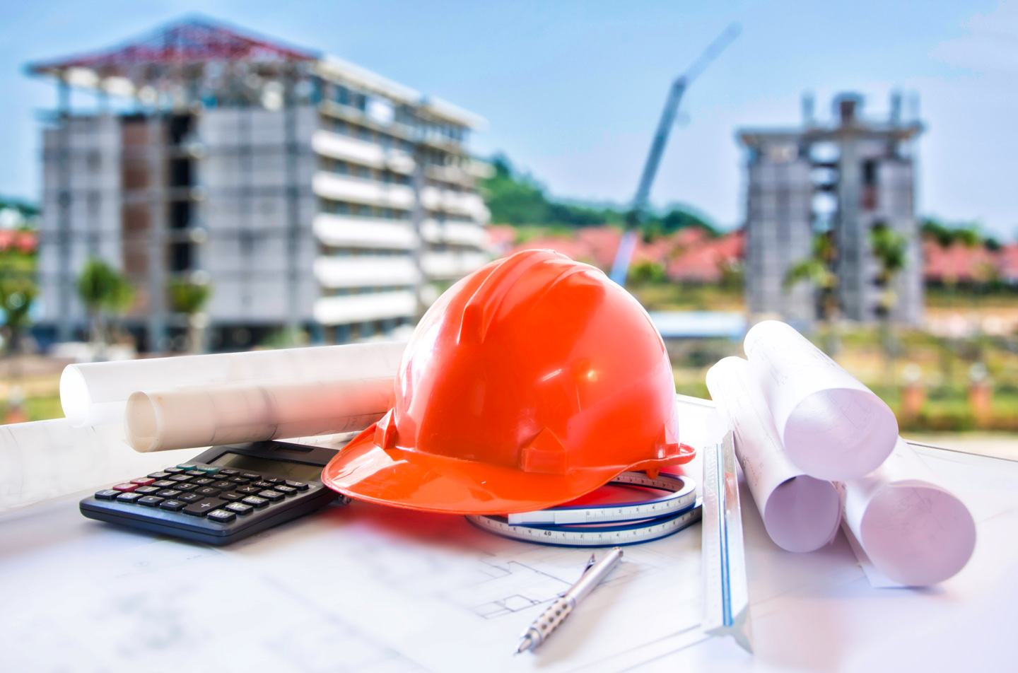 A construction safety helmet, calculator, and rolled up documents are on top of a table.