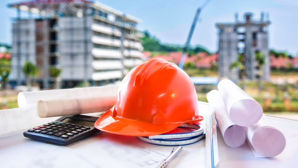 A construction safety helmet, calculator, and rolled up documents are on top of a table.