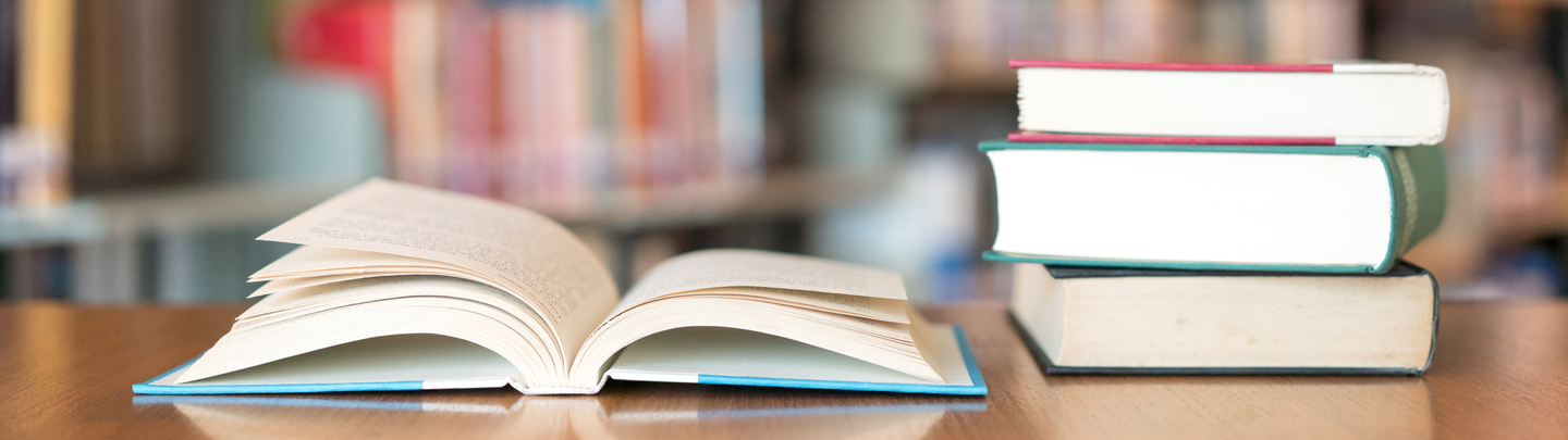 Stack of open and closed books with a blur bookshelf in the background