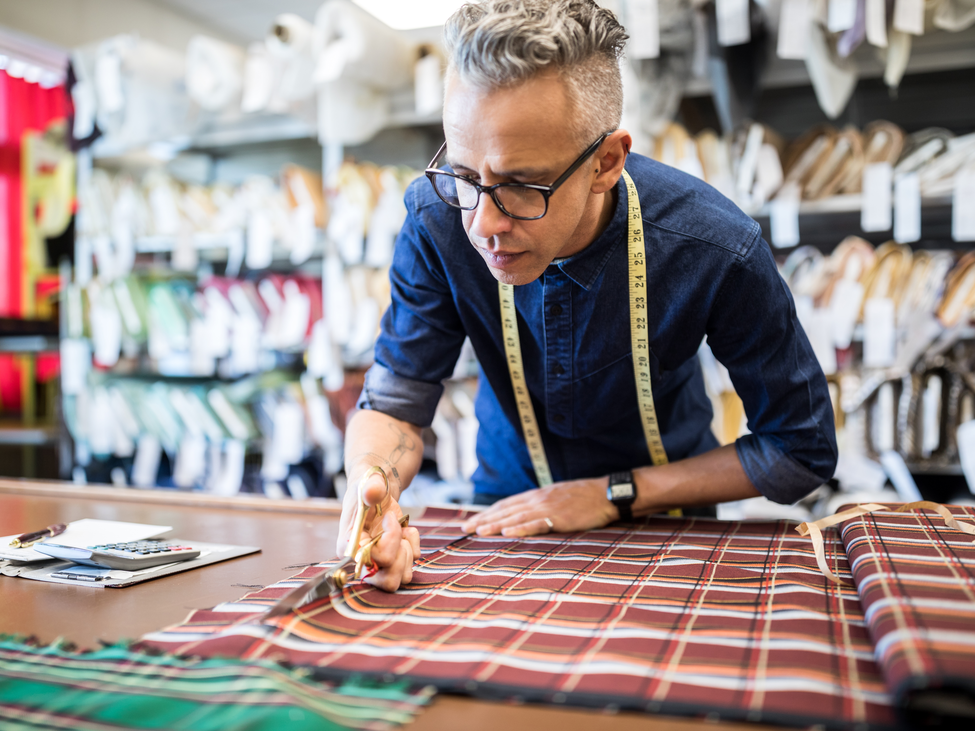 Tailor cutting a textile at workbench.