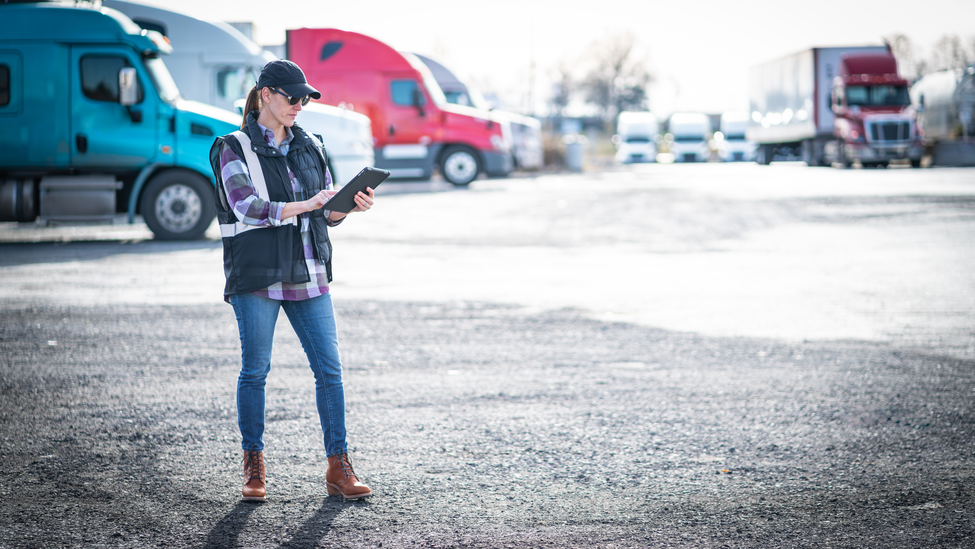 woman wearing sunglasses and hat standing in front of row of commercial trucks