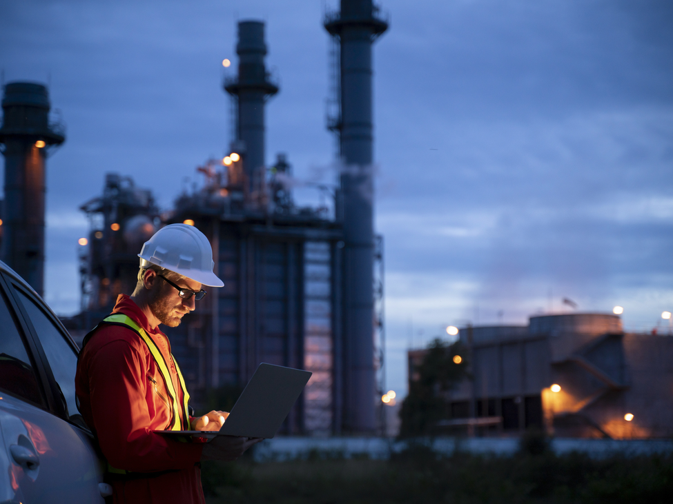 Oil refinery operator stands in the dusk outside a company facility.