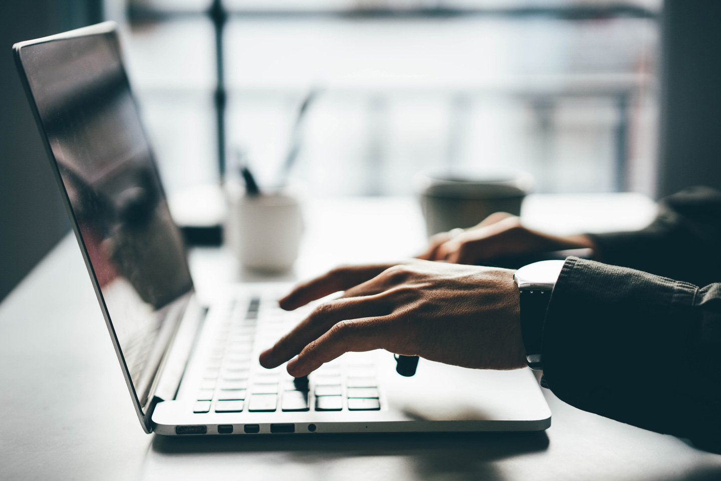 A man wearing a watch is typing on a laptop computer.