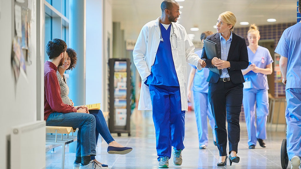 Employer talking to a doctor about safety while walking down the hall of a medical facility.