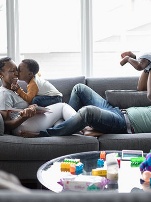 Couple playing with little boy and baby on sofa in living room.