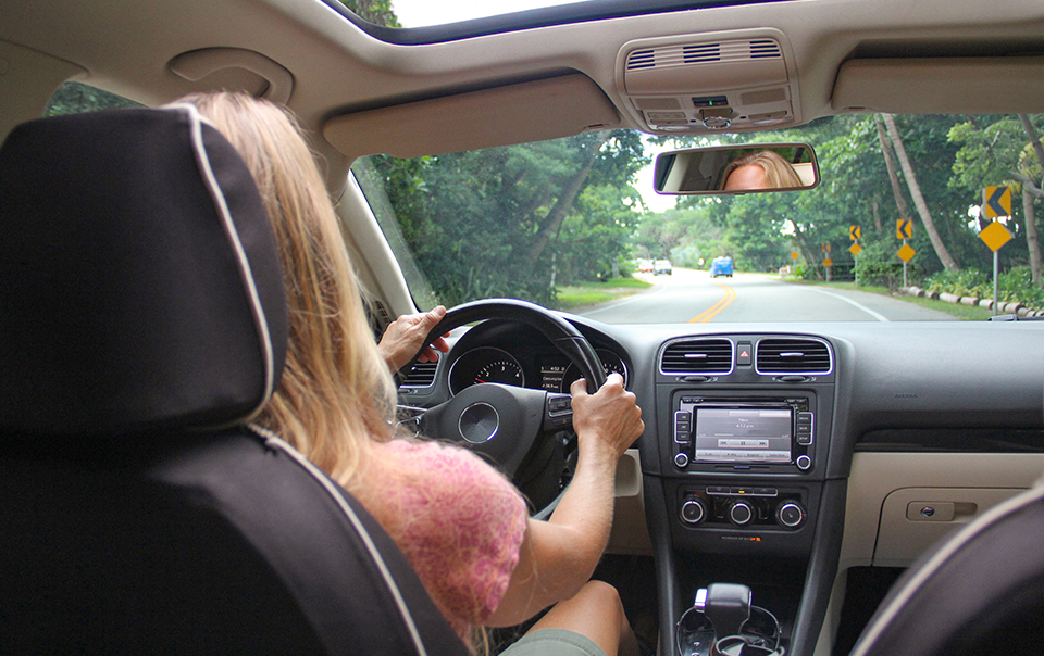 Image taken from back seat of a car of woman driving the car.