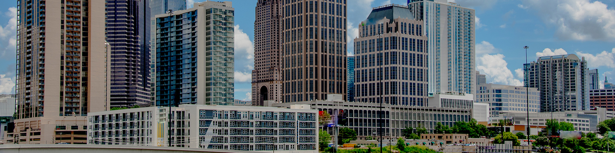 City skyline showing tall buildings against blue sky with puffy little clouds.