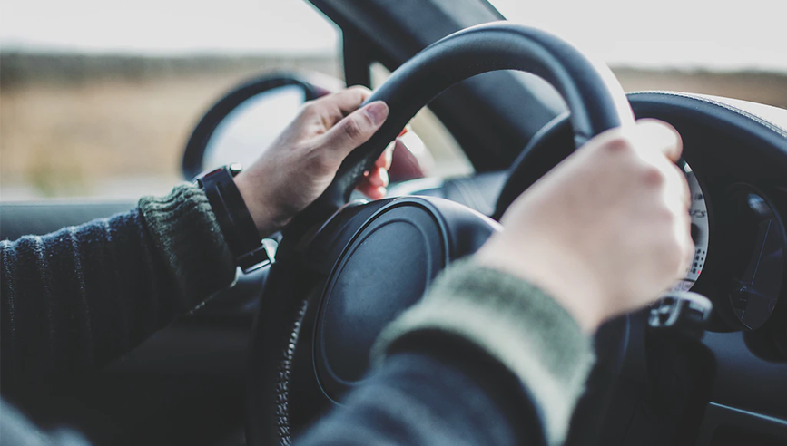 Man driving a car with two hands on the steering wheel.