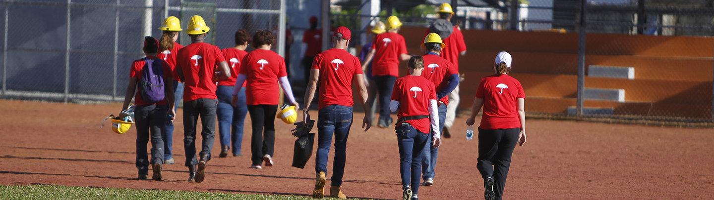 Men and woman volunteers wearing red tshirts with Travelers logo on backs and walking across a field.