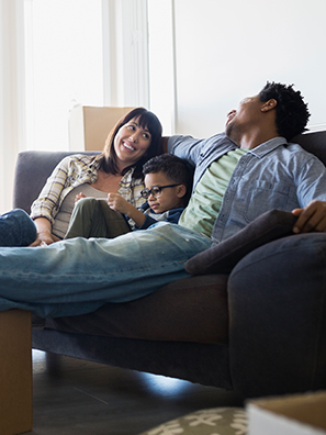 Couple and child relaxing on sofa, surrounded by moving boxes.