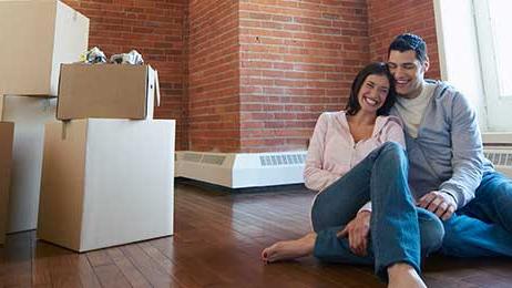 Two renters happily sitting on the floor of their new rental with moving boxes in the corner.