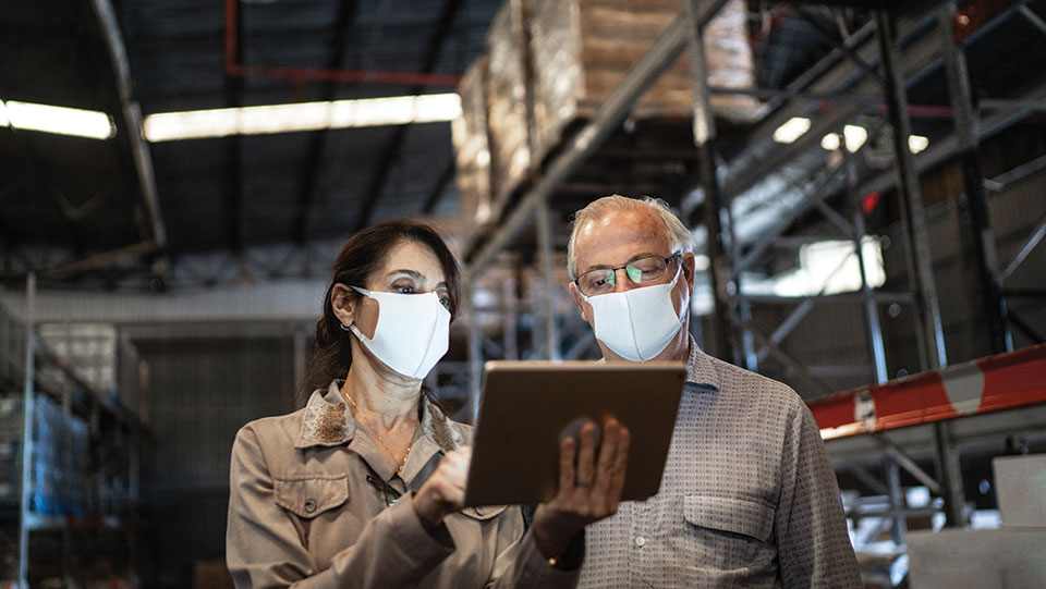 Two business insurance workers wearing masks looking at a computer in a warehouse.