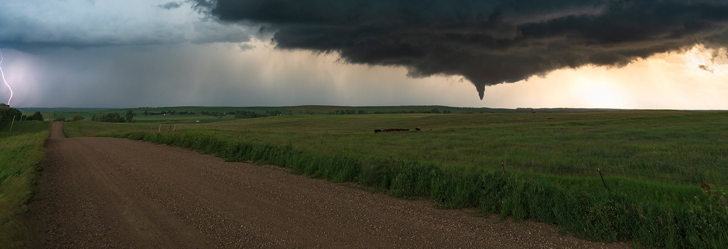 A tornado is seen in the distance across an open field.