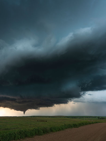 A tornado is seen in the distance across an open field.