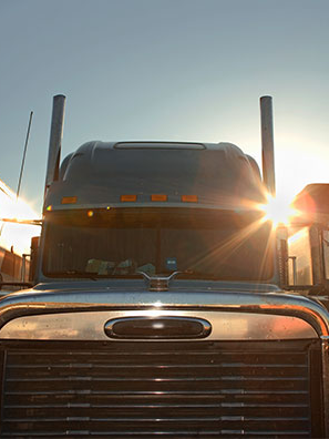 A row of three semi-trucks gleam with the sun rising behind them.