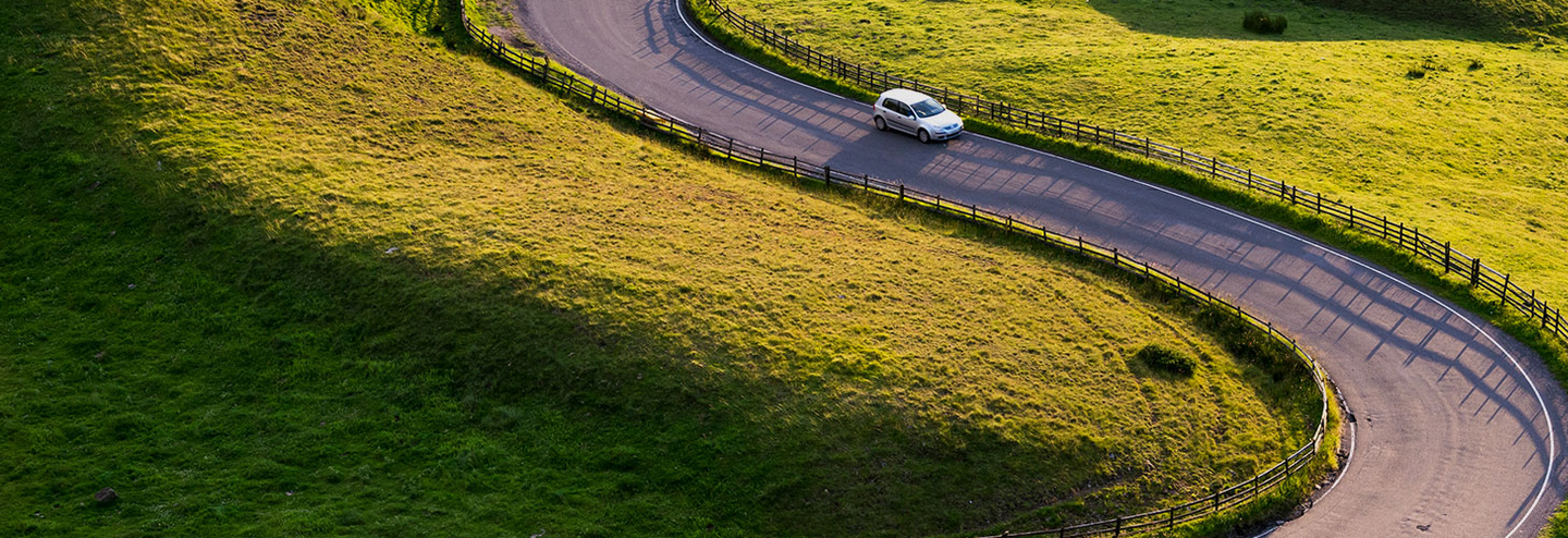 A car driving along a winding road in green fields.
