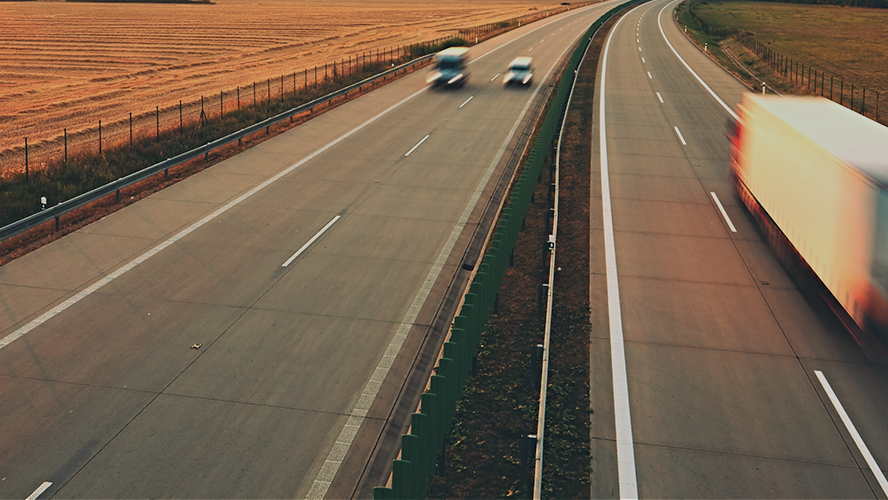 Long exposure shot of a rural highway with two cars traveling in one direction, while a semitruck travels away from the camera. 