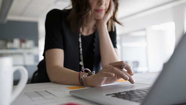 Woman using a laptop holding a pen in her hand.