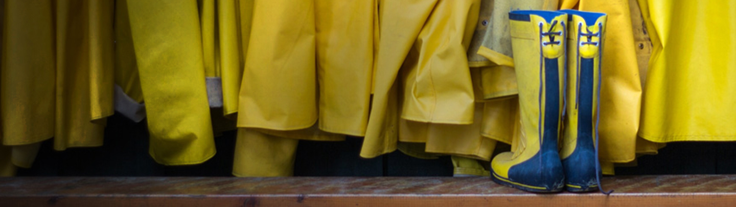 A set of rain boots sits on a bench next to several rain coats.