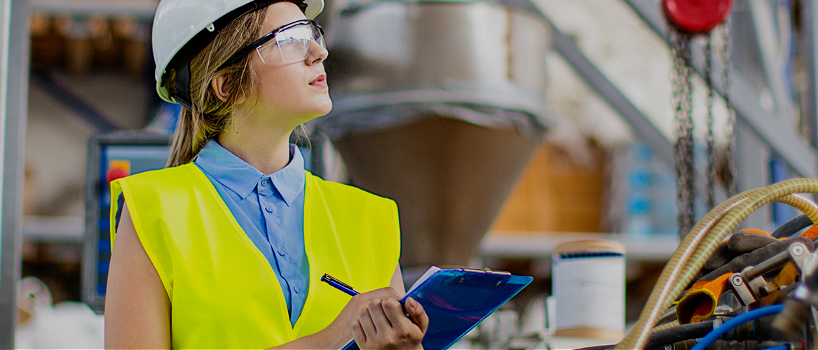 Woman in yellow safety vest holding clipboard managing a facility.